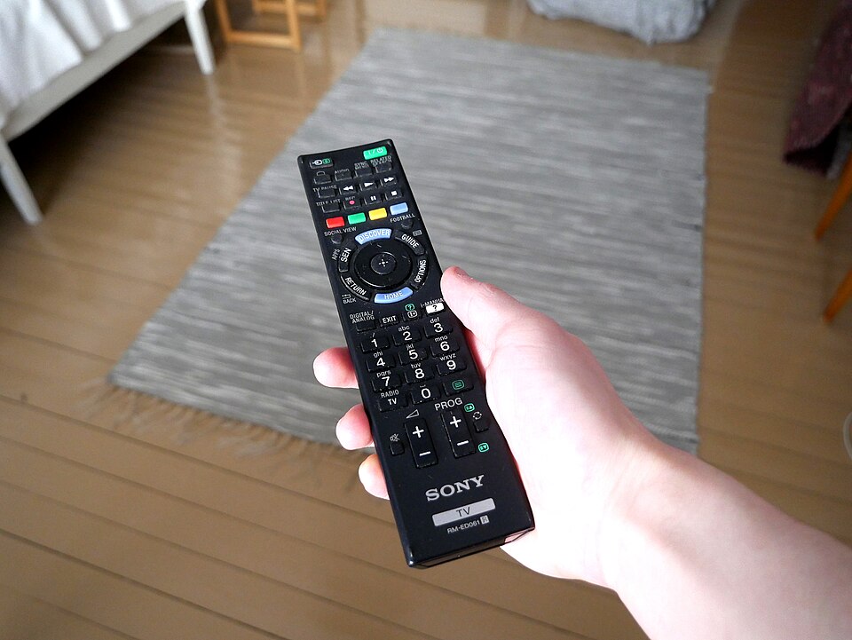 Persoana care tine o telecomanda in mana in timp ce cauta canale romanesti gratis pe televizor