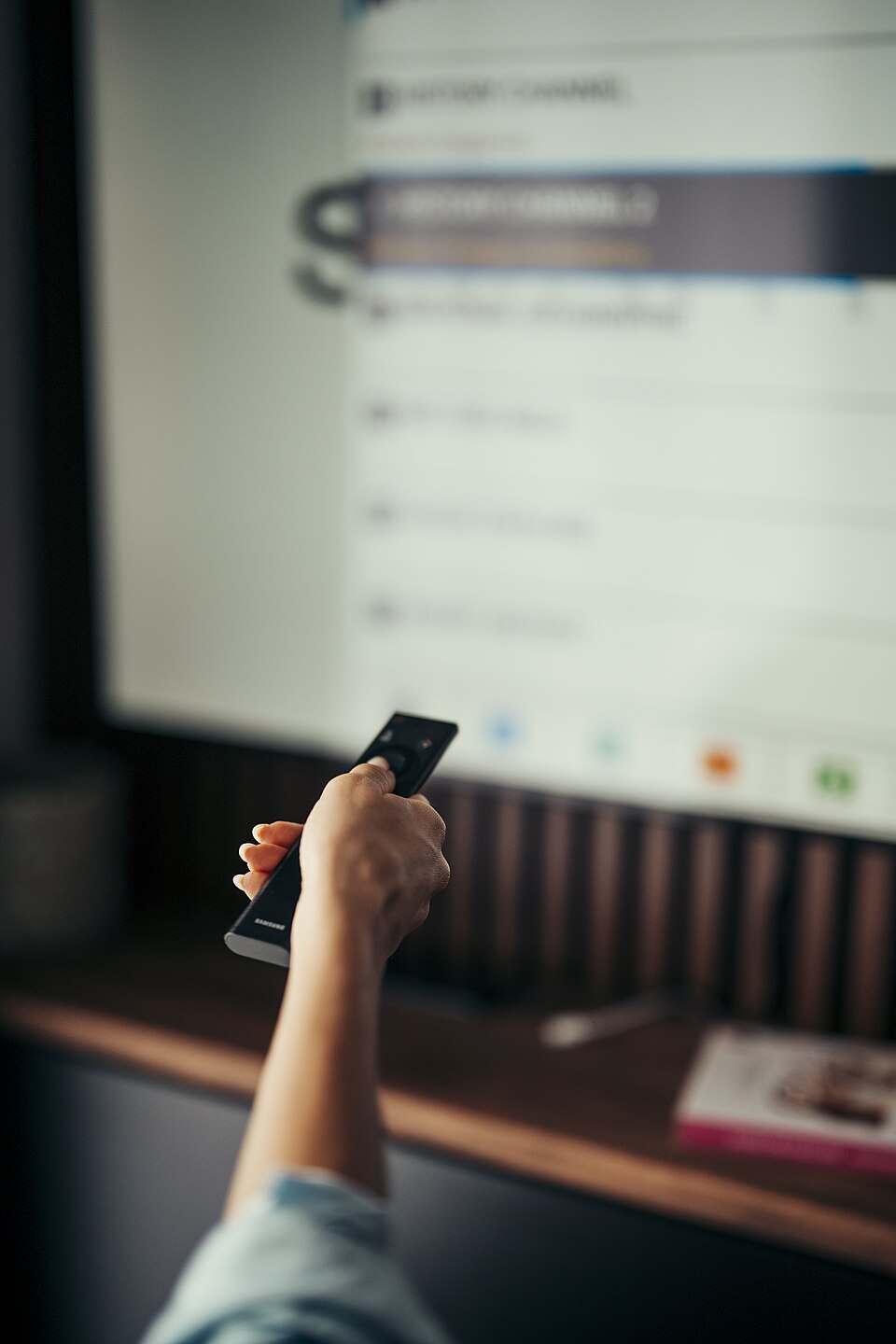 Persoana care tine o telecomanda in mana in timp ce cauta canale tv gratuit pe televizor
