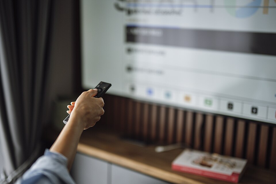 Persoana care foloseste telecomanda pentru a naviga in meniul aplicatiei IPTV pe televizor, cautand o lista iptv romania m3u
